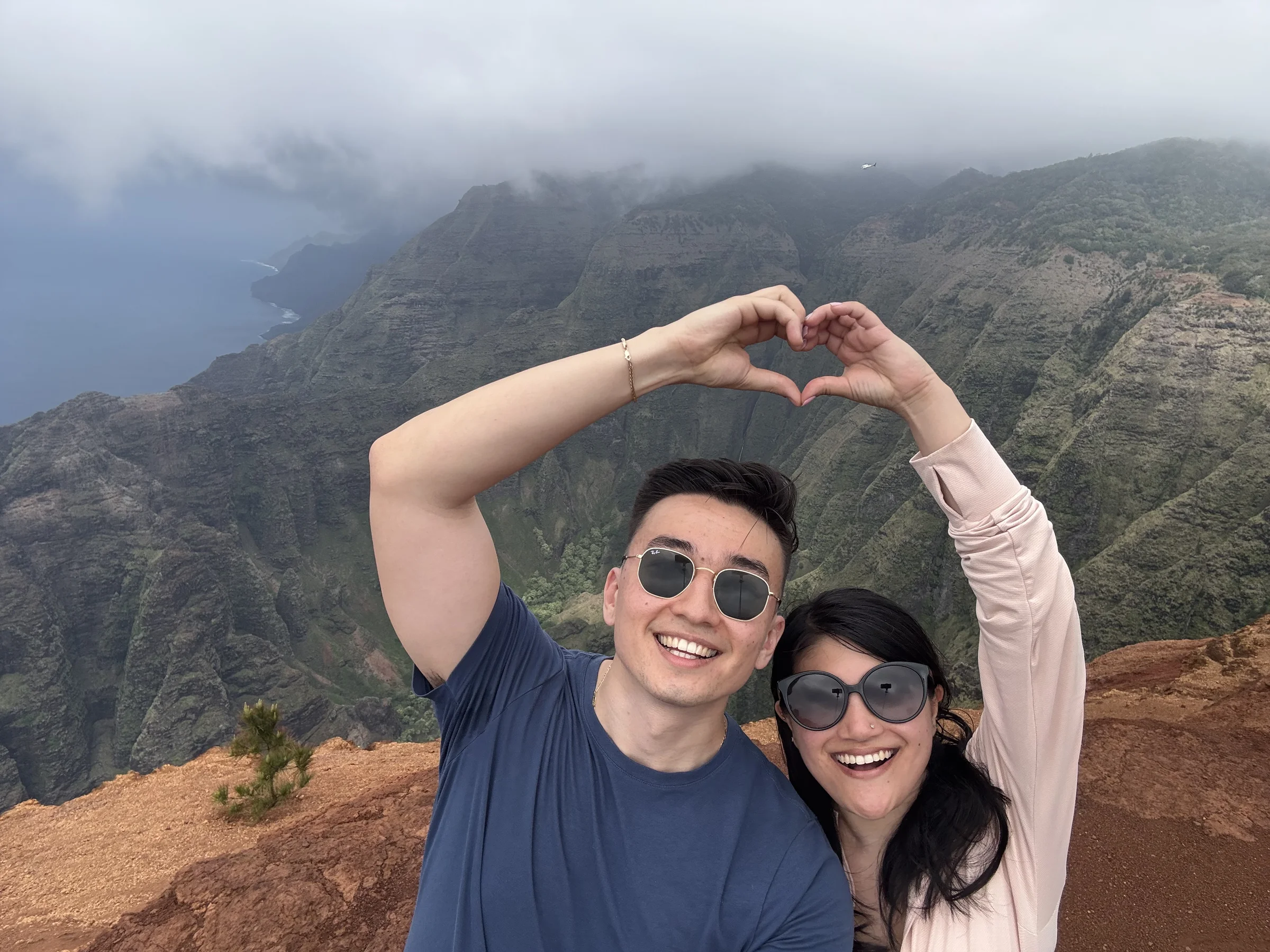 Olivia and Geoff at Kauai, making a heart with their hands over the valley